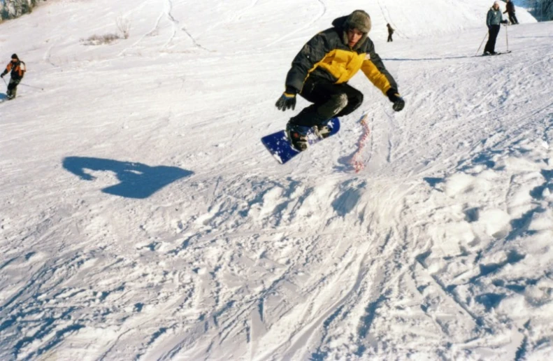 a man in a yellow jacket jumps down on his snowboard