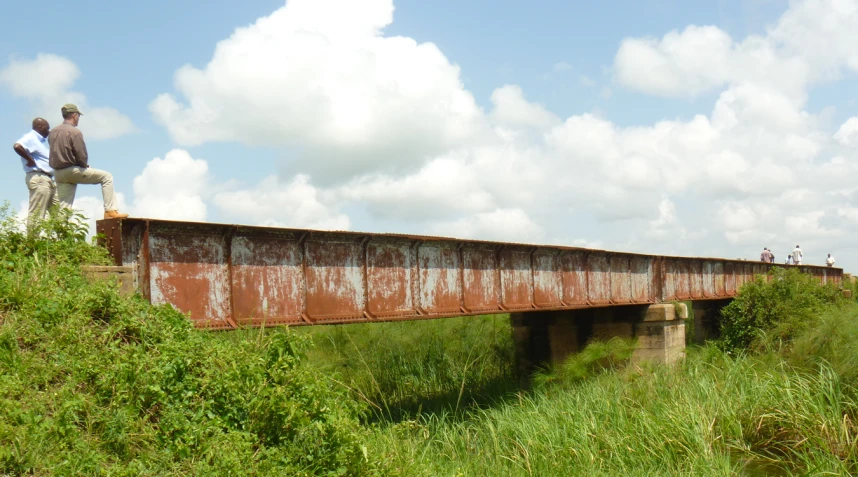 two men standing on an old rusted bridge in a field