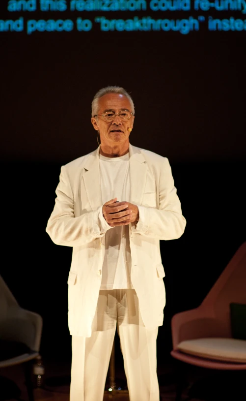 an older man standing on stage wearing a suit