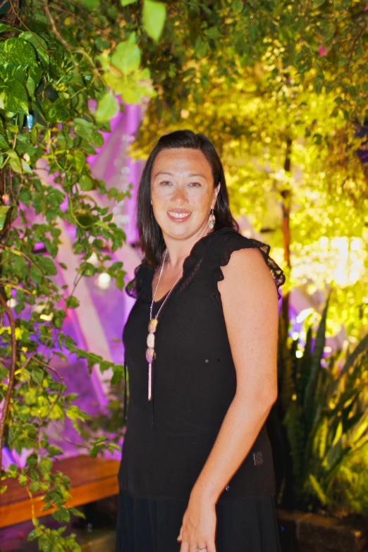 woman in black dress smiling as she stands near trees