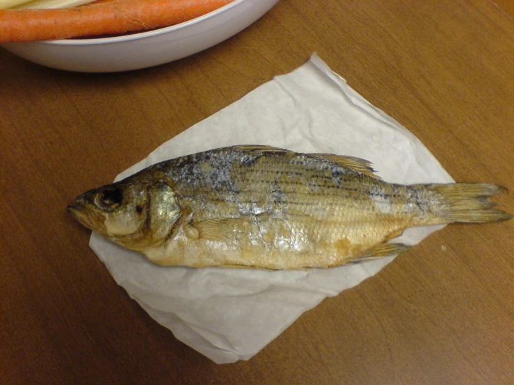 a small fish is laying on a piece of parchment paper next to carrots