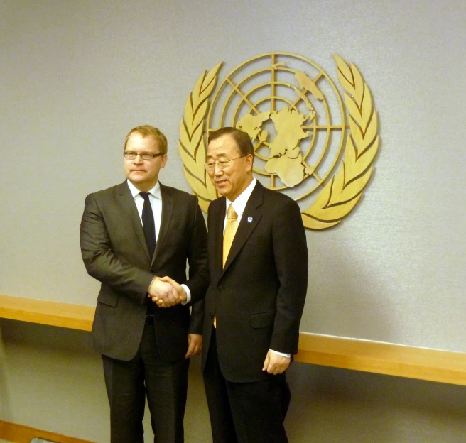 two men in suits stand by the un logo