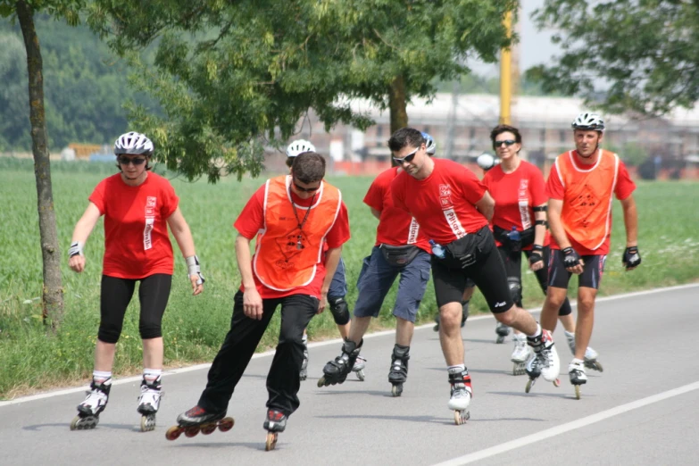 several people skateboarding down the road and wearing orange shirts