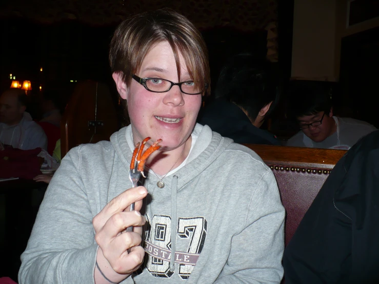 a woman with glasses smiling while holding up a piece of food