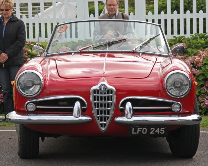 a red car parked beside a woman with sunglasses