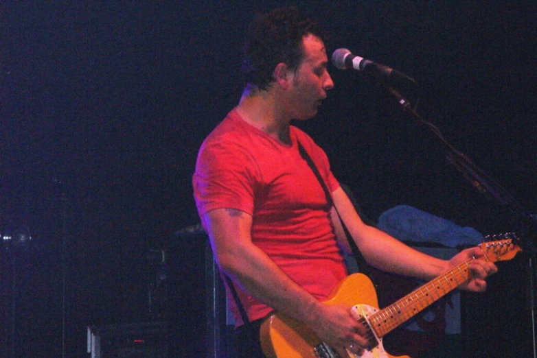 a man with red shirt and guitar on stage