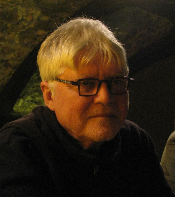 a man wearing glasses and a black shirt looking down at soing