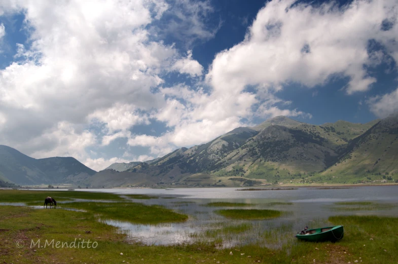 a boat on the lake in a field with mountains in the background