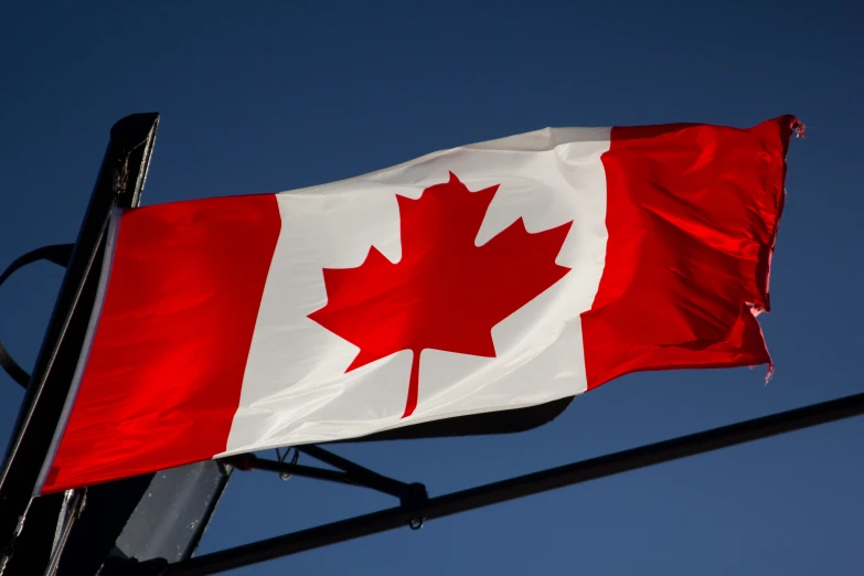 a canadian flag flying in the wind with blue sky behind