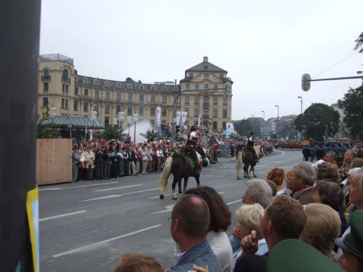 people watch as two horses are walking down the street