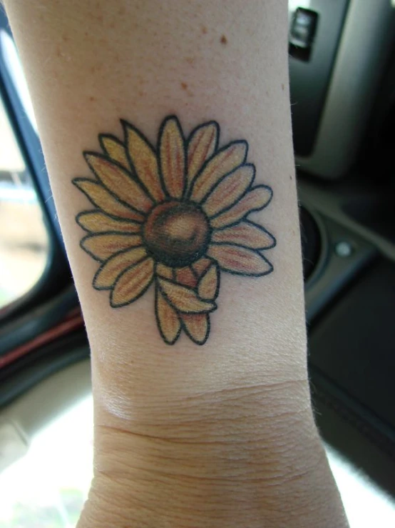 a womans foot is holding a tattoo with a daisy on it