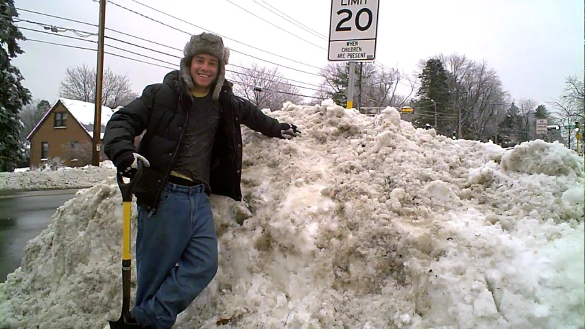 a young man poses for a picture in front of a huge pile of snow