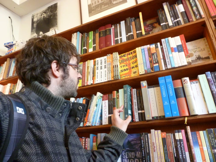 a man with glasses and beard standing in front of a book case
