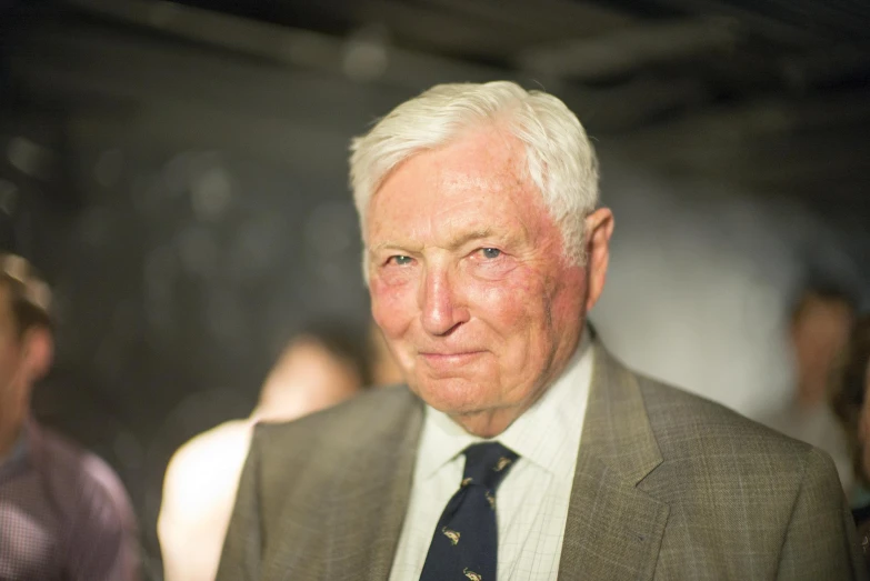 a older man in suit and tie standing close to some people