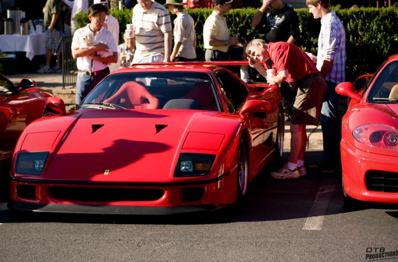 a red ferrari parked next to another one with people looking at it