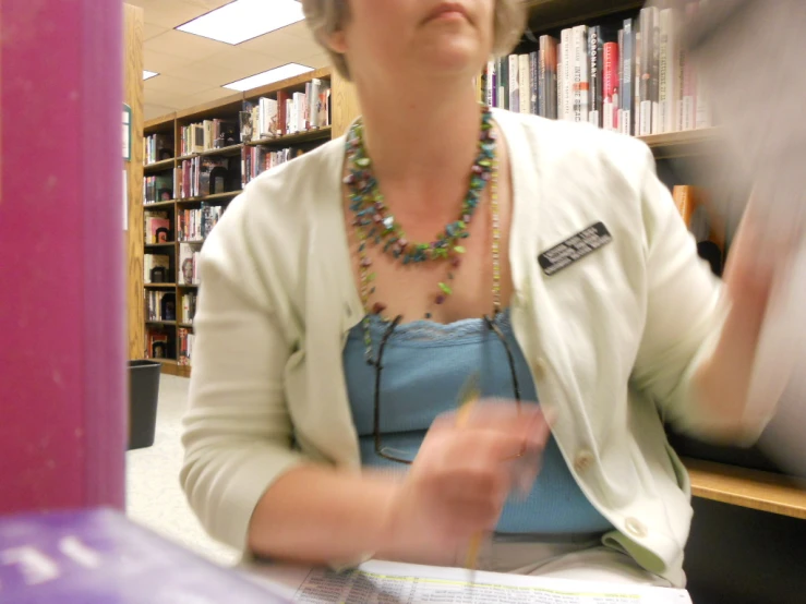 a woman sitting at a table in front of a book shelf