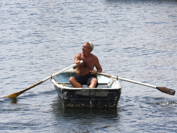 a shirtless man rowing a boat on water