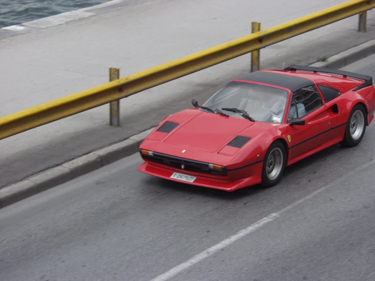 a red sports car drives down a highway next to the ocean
