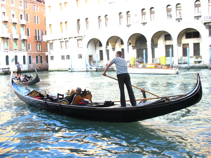 a man stands on the back of a boat while two others ride by in a gondola