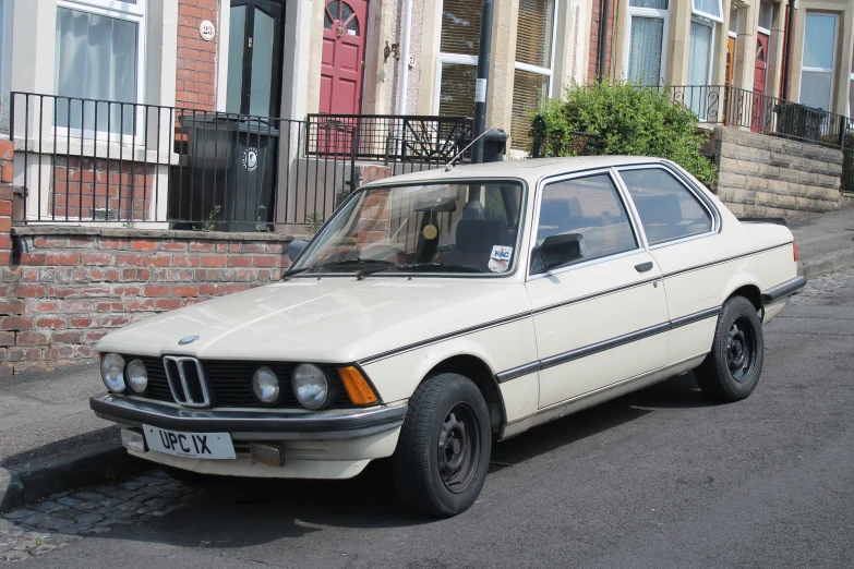 an old beige bmw sitting on the side of the road