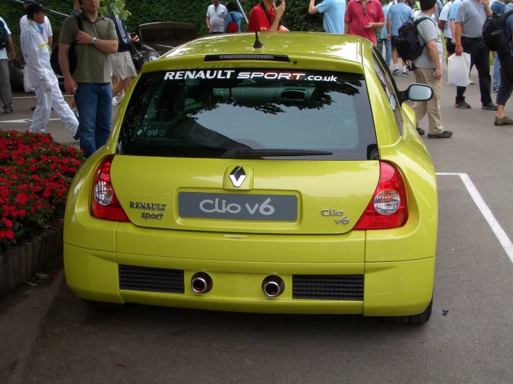 a small yellow car driving on the road near people