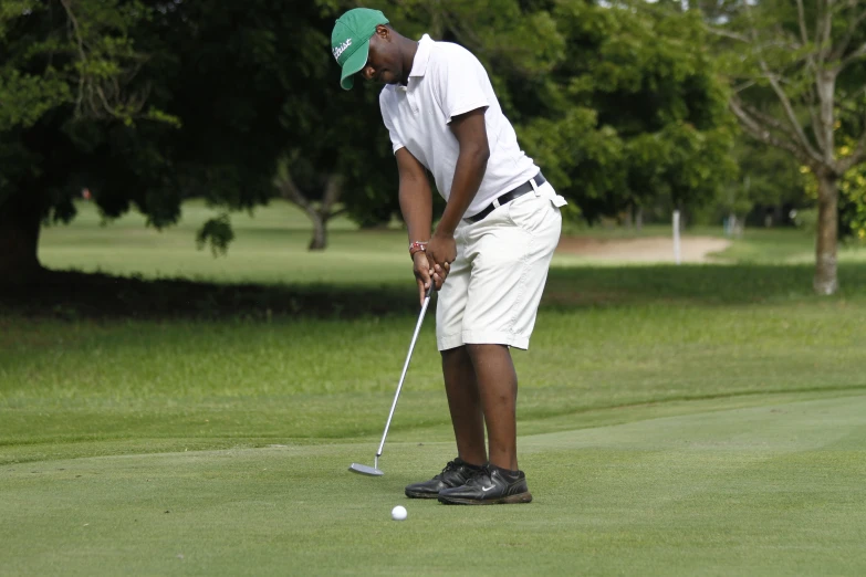 man playing golf in white shorts and a cap