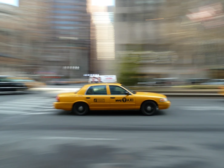 yellow cab driving past tall building with sky in background