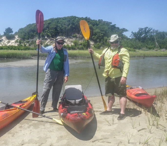 a man and woman standing in the sand next to some kayaks