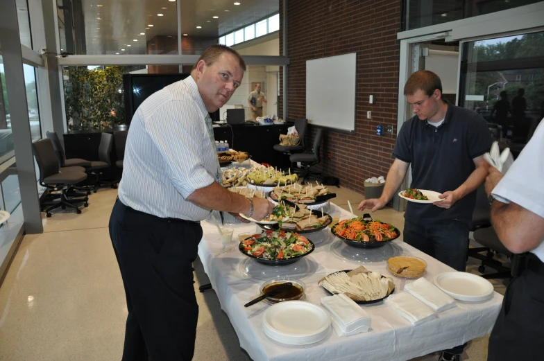 three men stand next to a long table covered with food