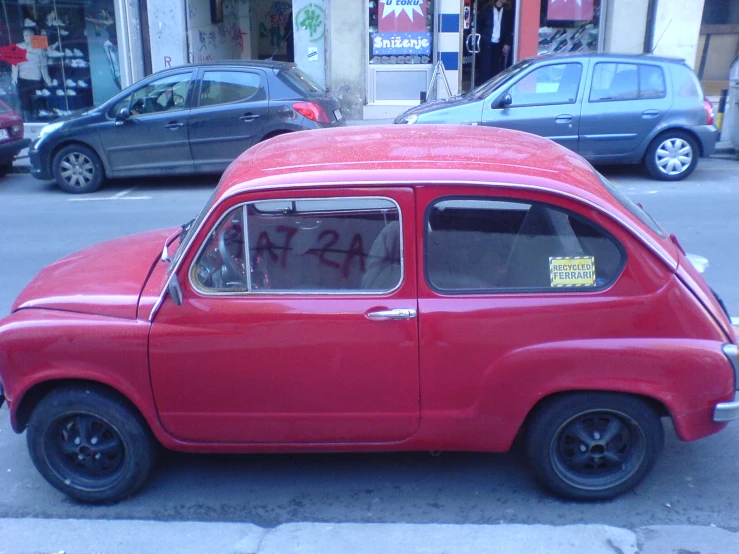 an old red car parked next to a busy city street