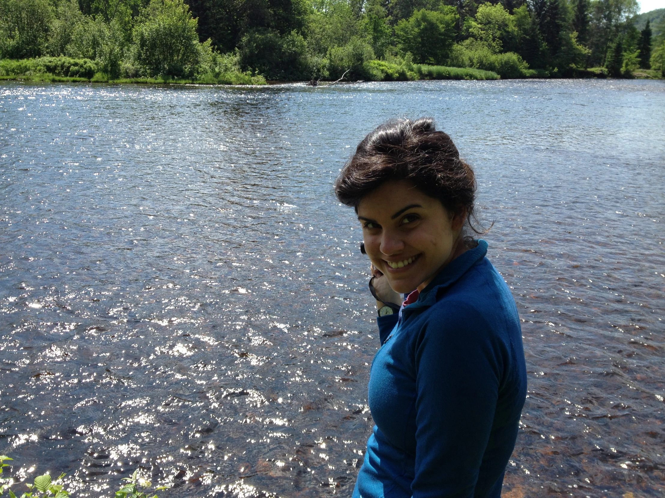 woman standing next to body of water with trees and brush on it