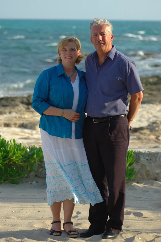 a man and woman are standing on the sand in front of the ocean