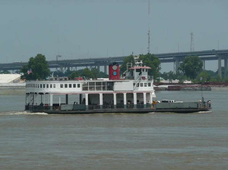 a large ferry on the water with trees and bridges behind