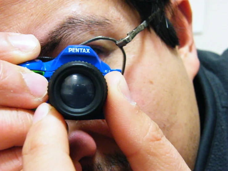 a man looking through a blue camera with the lens up to his face