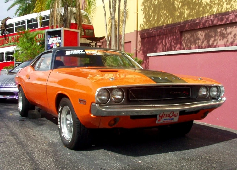 an orange muscle car parked in front of a double decker bus