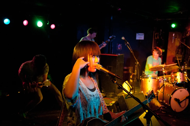 three young women singing with one playing the guitar