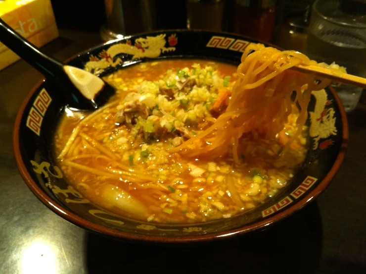 a bowl filled with noodles, meat and soup on top of a table
