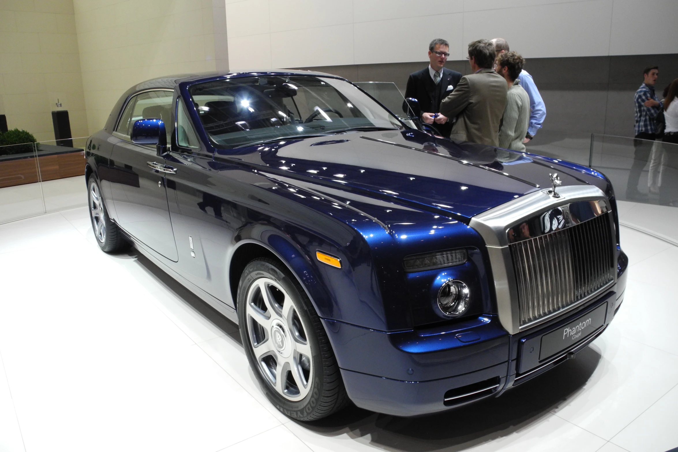 a rolls royce parked on a white floor with people