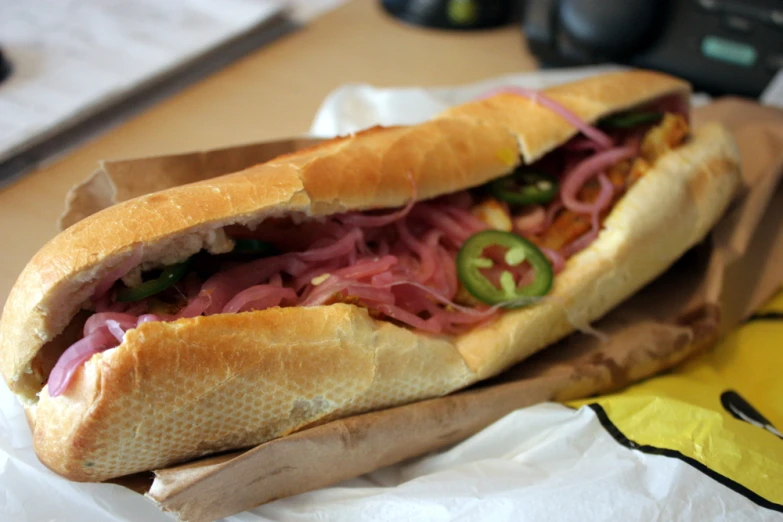 a sub sandwich with onions and lettuce sits on wax paper