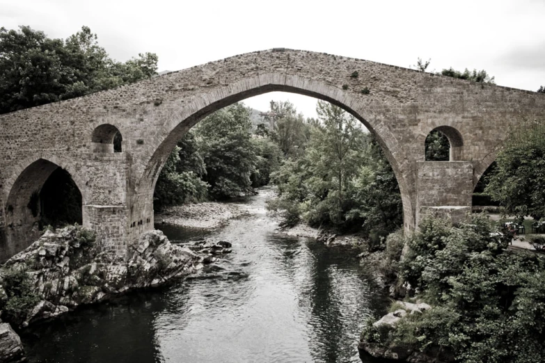 an old stone bridge is crossing over a small river