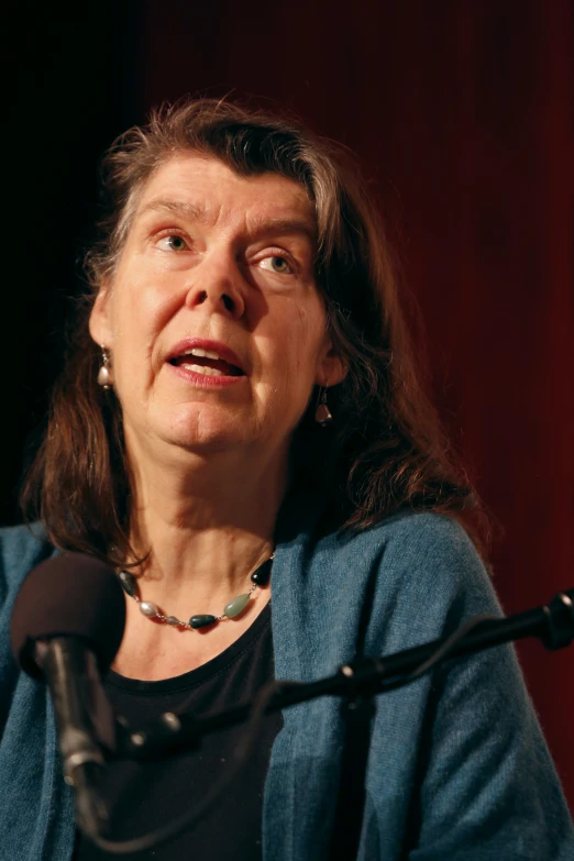 a woman with long hair sitting at a microphone and talking