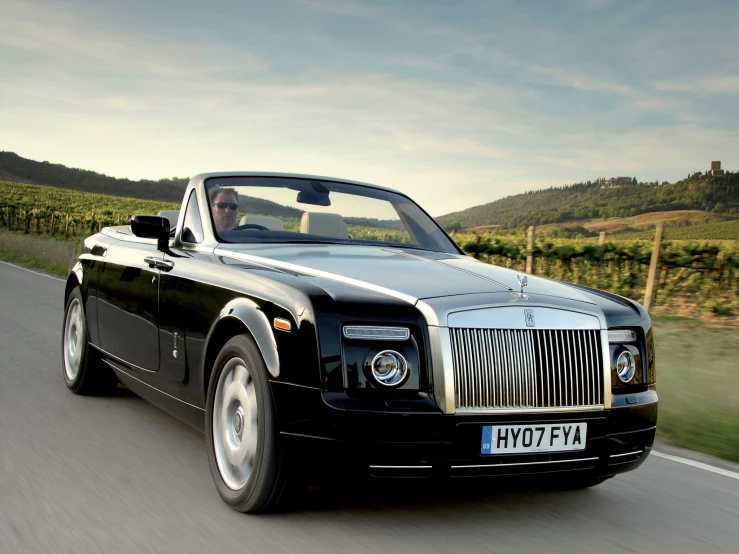 a rolls royce with an open convertible cab driving down the street