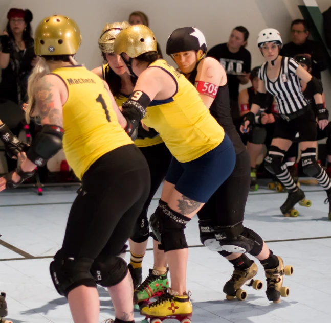 three female roller skaters dressed in yellow and black in an indoor rink