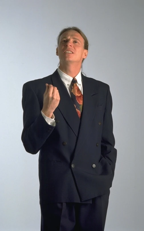 man in a suit making an obscene face while holding his hand up