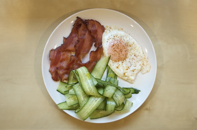 a plate of food with bacon, cucumber and eggs