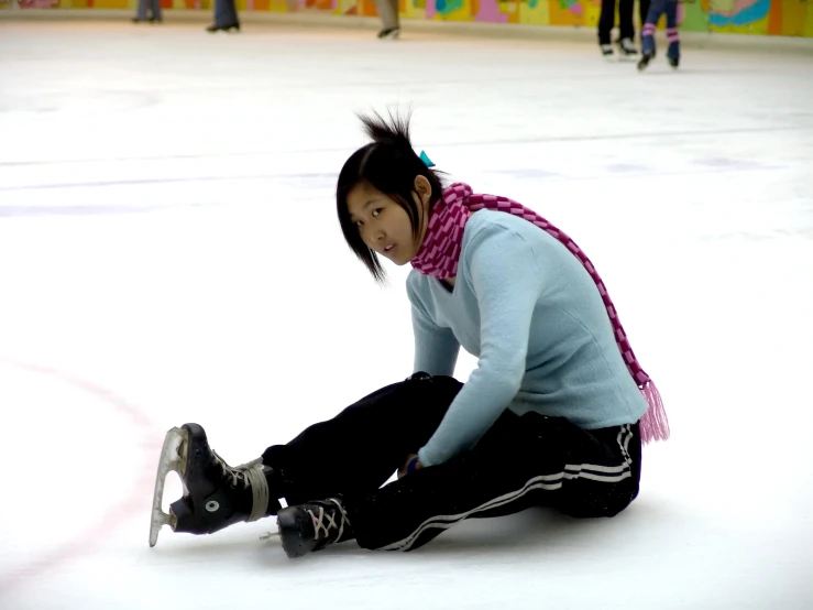 an asian woman crouched down on the ice as she performs a stunt