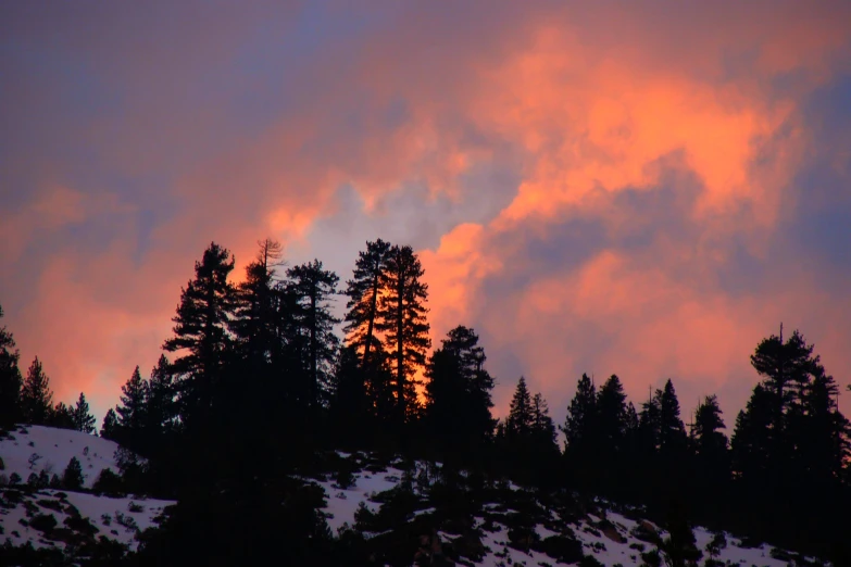 red, yellow and orange clouds over tree tops on snow covered hill