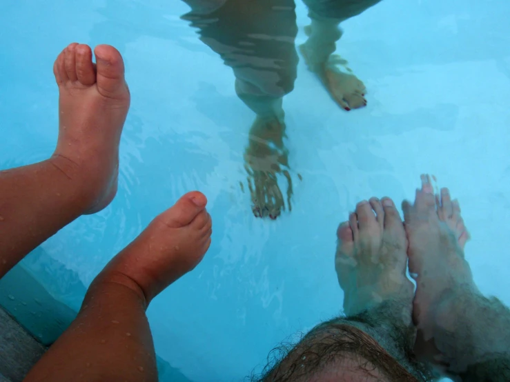 a group of feet in the pool water with their reflections