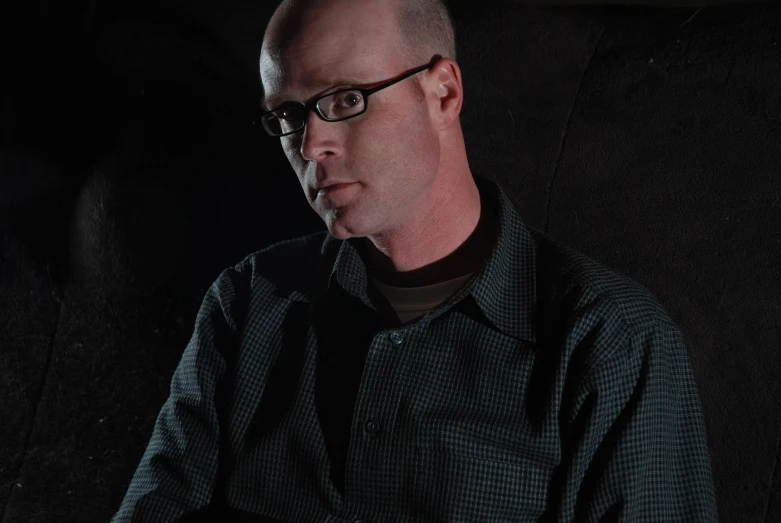 a man with glasses sitting against a black background