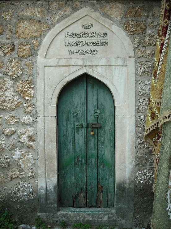 a green door in a stone building with writing on the side
